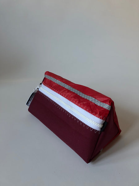 Trianglar shaped storage case for toiletries, and essentials for travel. Sits solidly on surface. Wrist strap made of webbing and heavy duty zip. Lined.